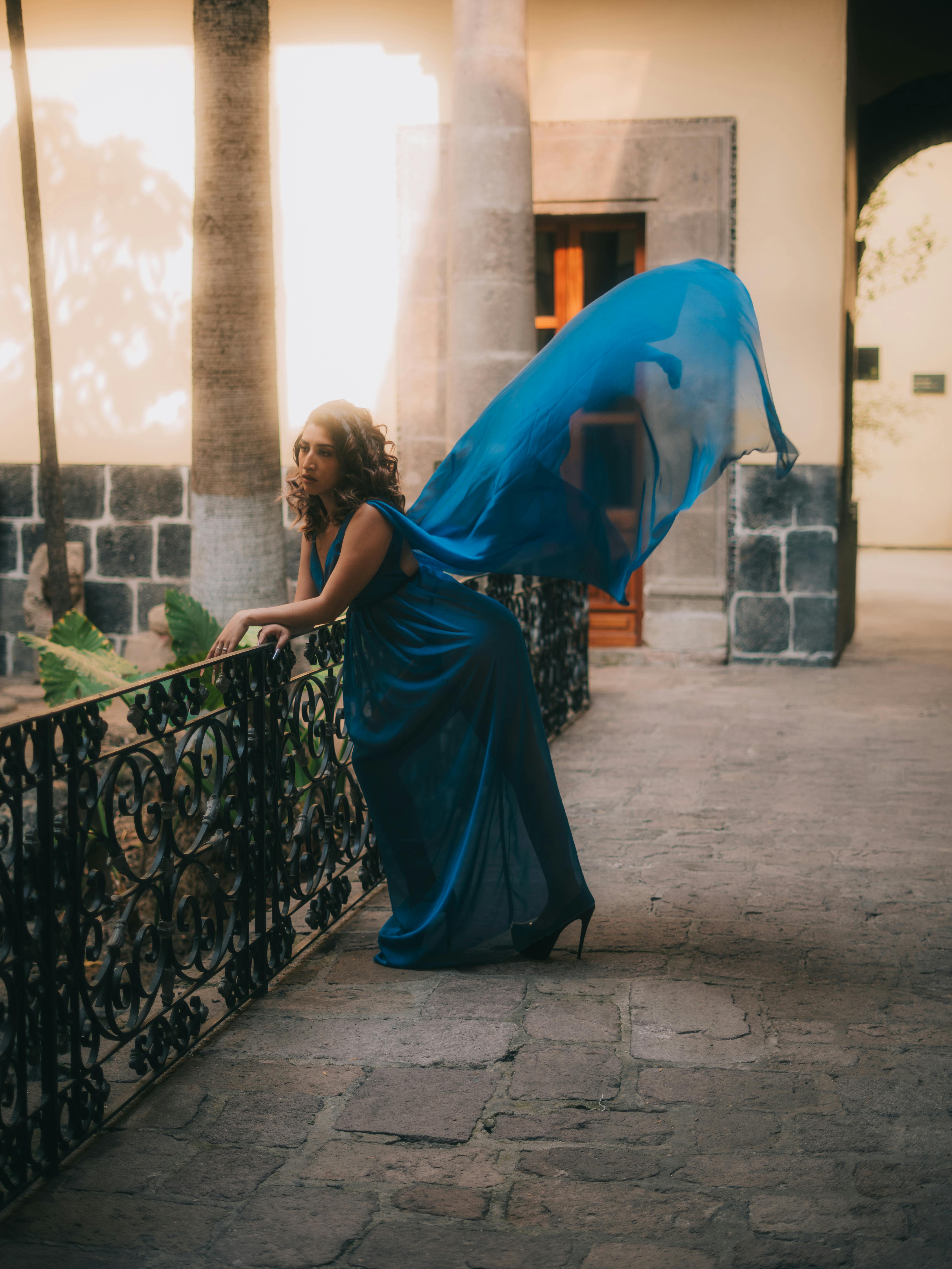 De franc Dona elegant amb un vestit blau fluid posant artísticament en un entorn històric del pati. Foto d'estoc
