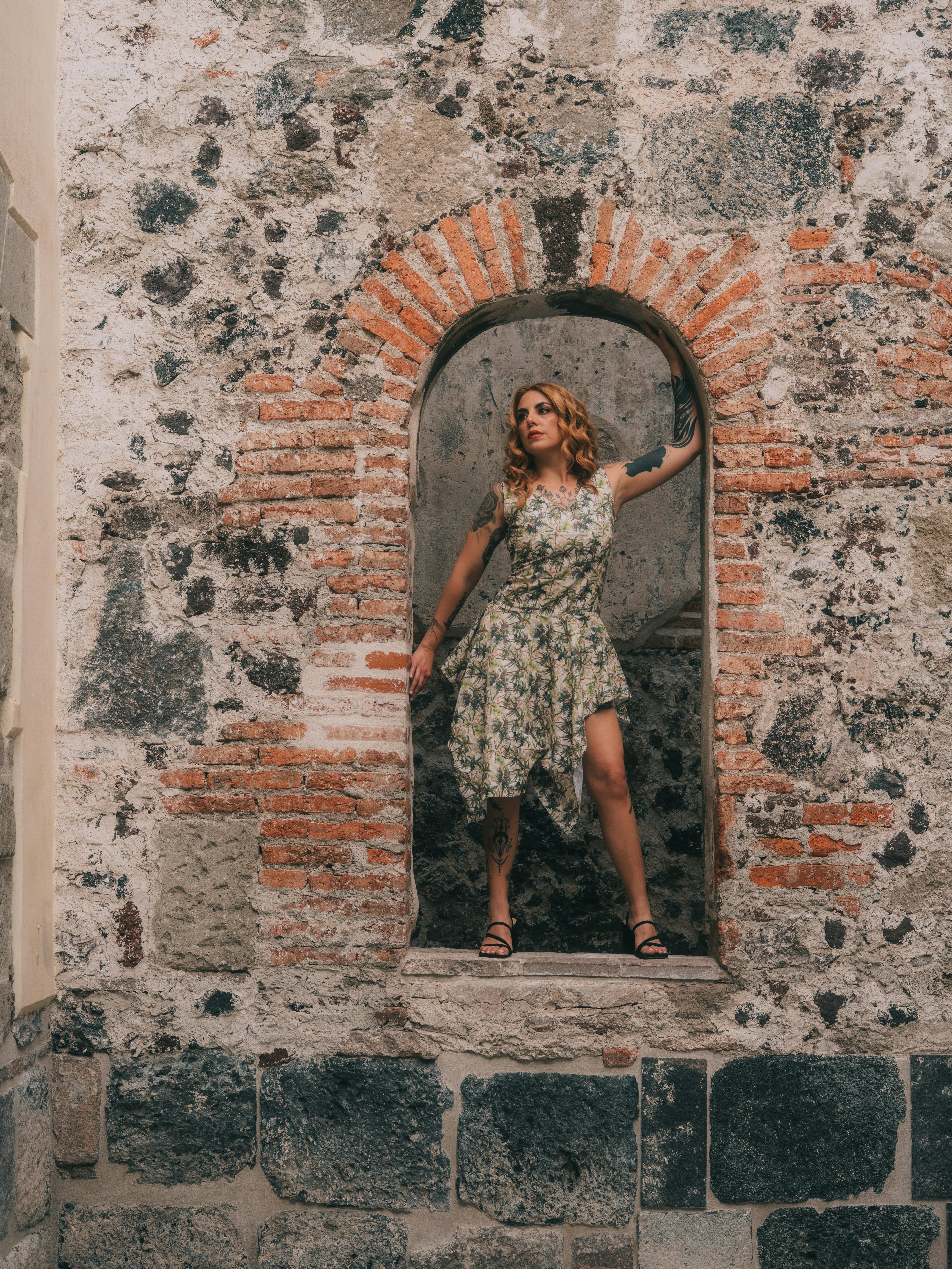 Gratuit O femeie într-o rochie florală pozează elegant într-o arcadă rustică din piatră. Fotografie de stoc