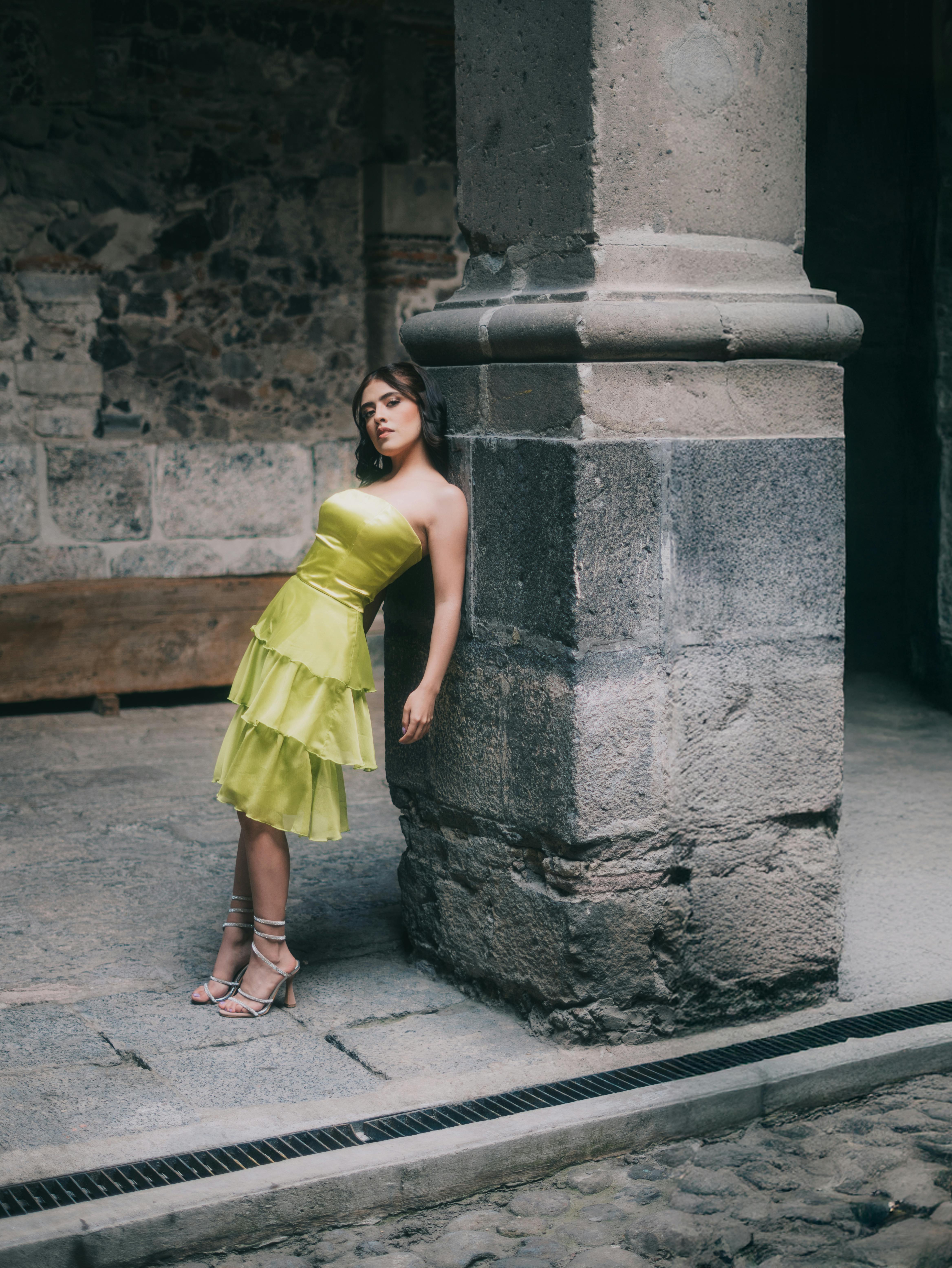 Free Elegant woman in lime green dress leaning against a column in a historic building in Mexico City. Stock Photo