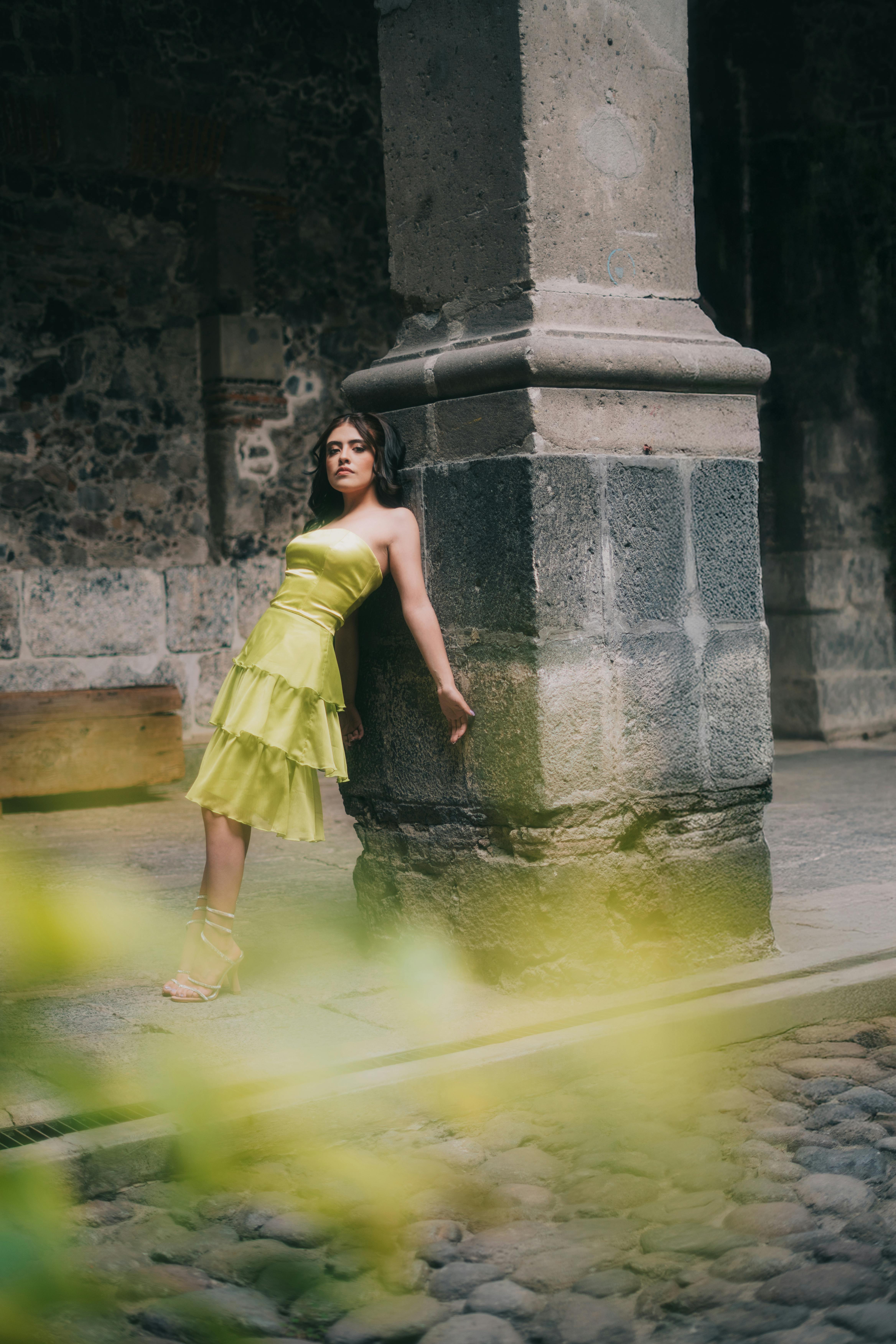 Free Stylish woman in lime green dress leans against column in historic courtyard in Mexico City. Stock Photo