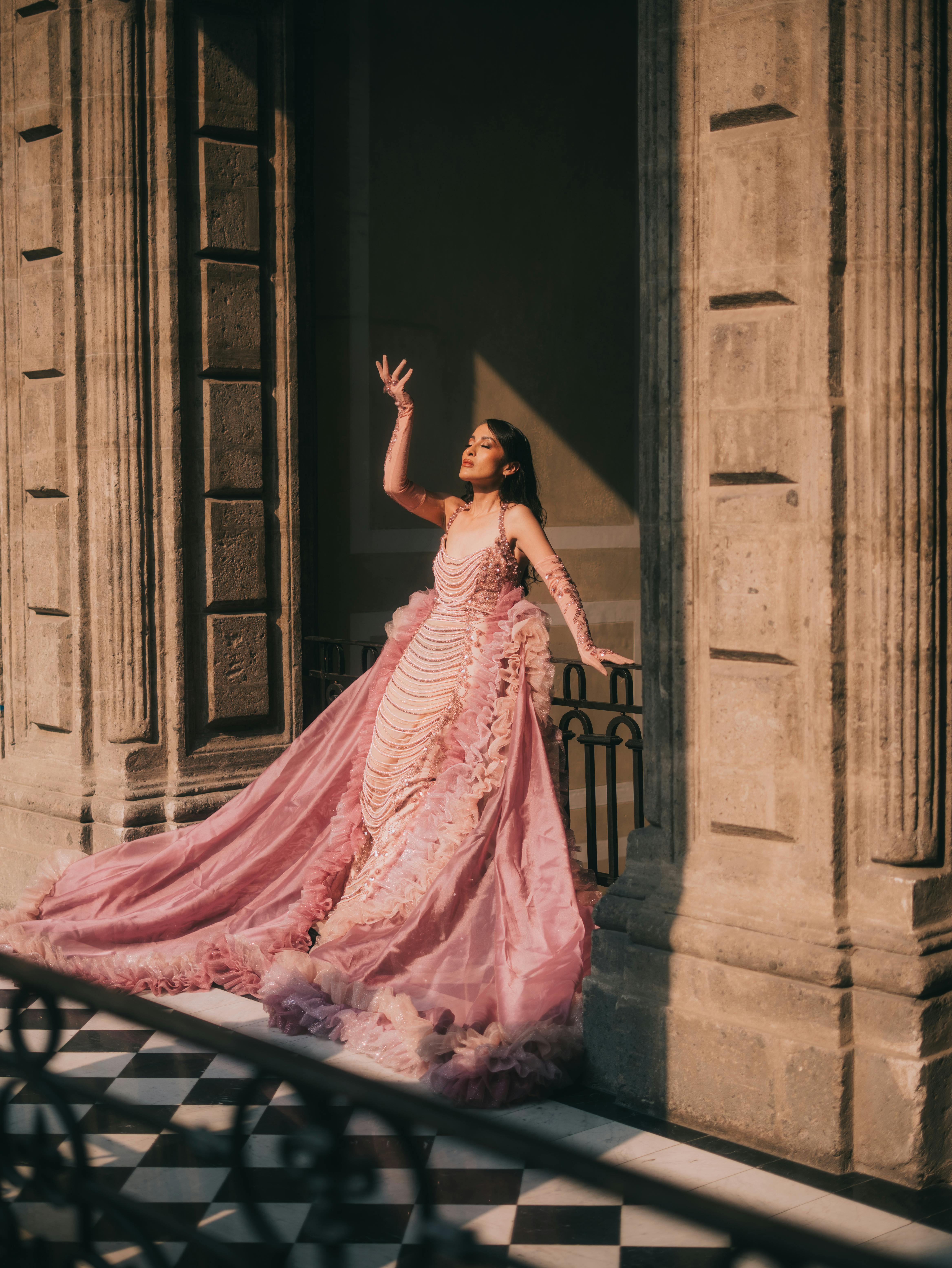 Free Elegant fashion model poses in a luxurious pink couture dress against a historic Mexican building. Stock Photo