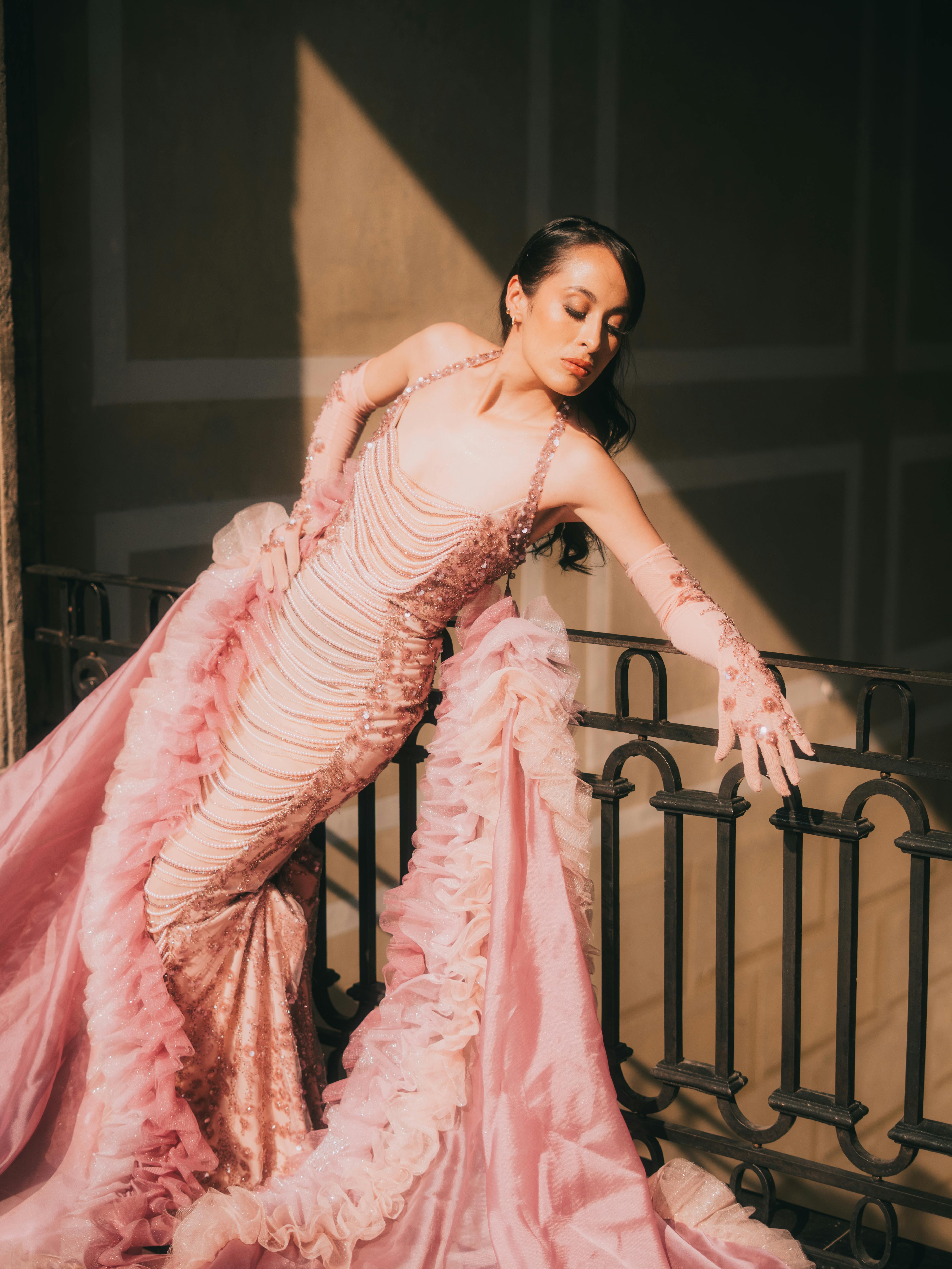 Gratis Modelo de moda con un elegante vestido rosa con volantes posando en el interior frente a una barandilla ornamentada, exudando sofisticación. Foto de stock