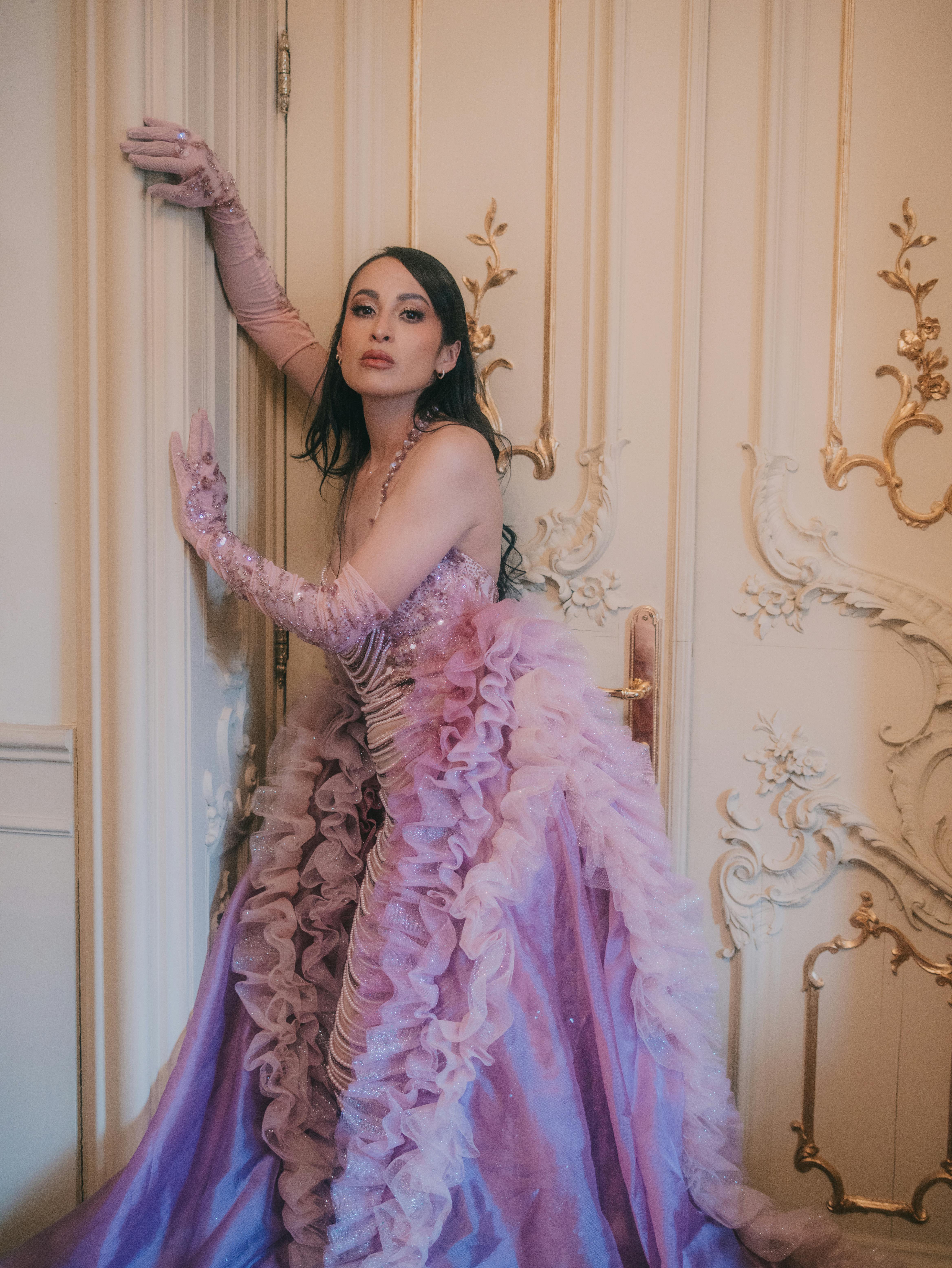 Gratis En sofistikeret model i en luksuriøs lilla kjole poserer elegant inde i et udsmykket rum. Lagerfoto