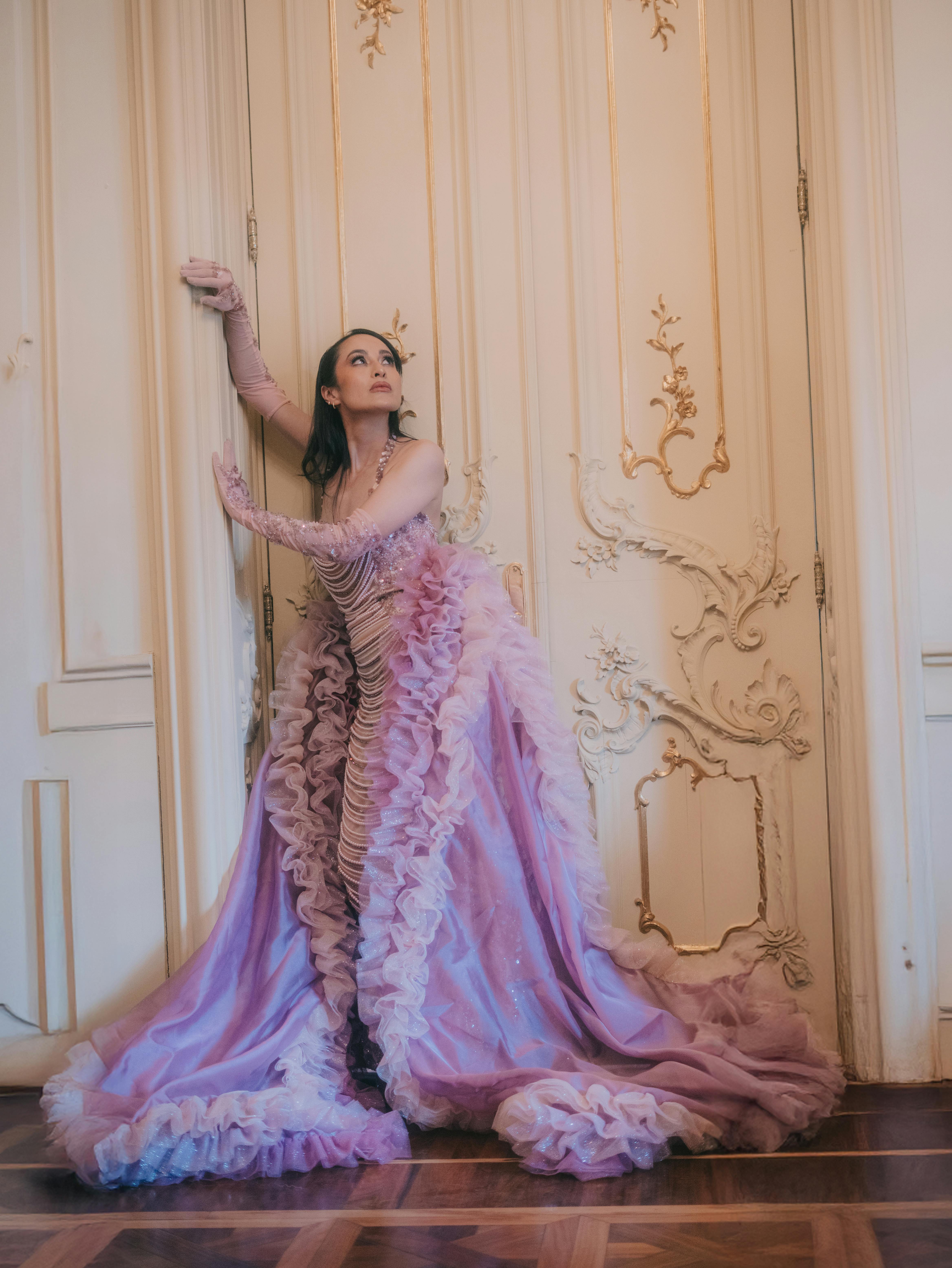 Kostnadsfria En modell i en rosa klänning poserar konstnärligt mot utsmyckade dörrar och visar upp elegans och mode. Stock foto