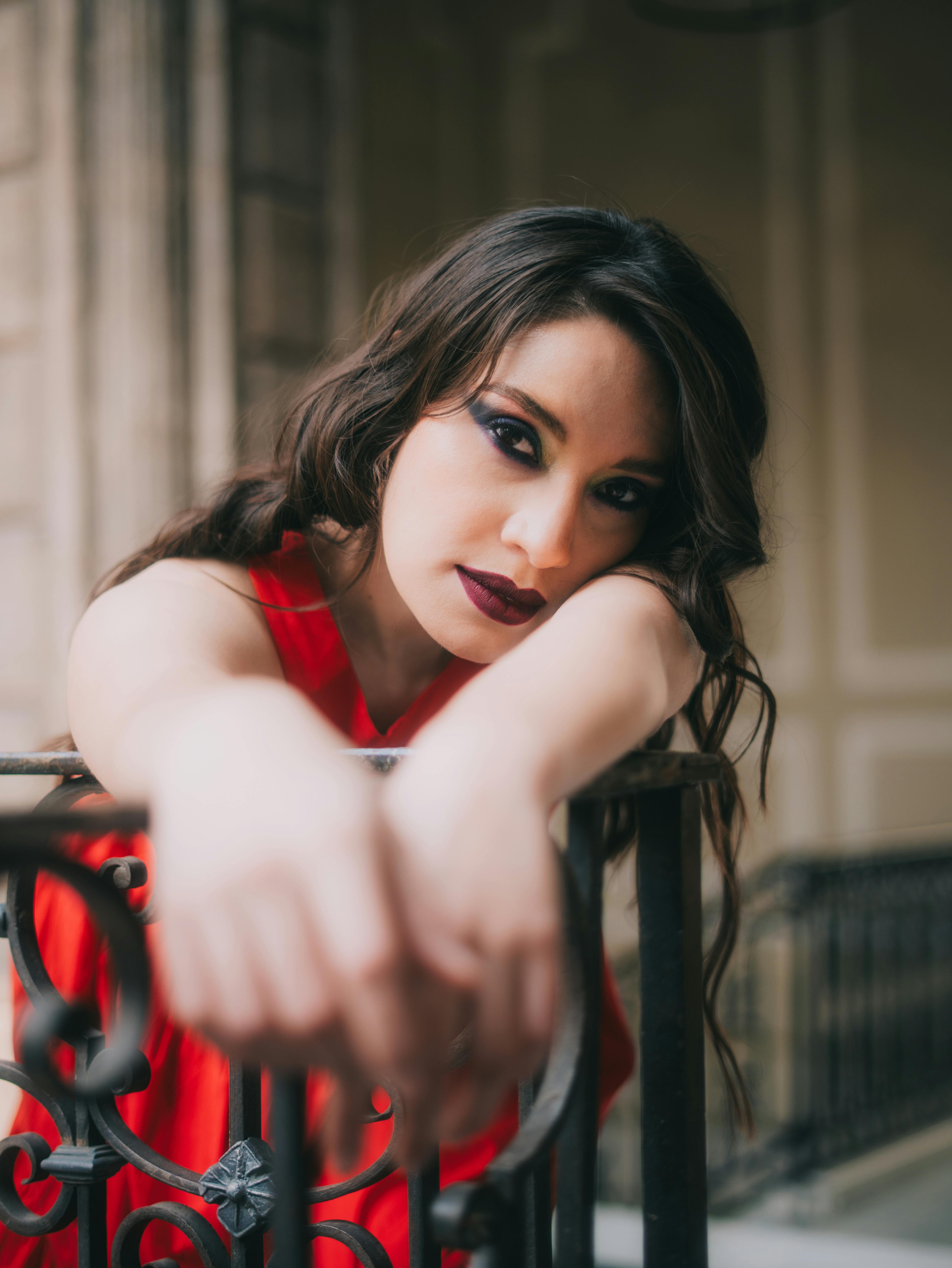 Kostenlos Elegante Frau in einem roten Kleid posiert mit auffälligem Make-up auf einem historischen Balkon. Stock-Foto