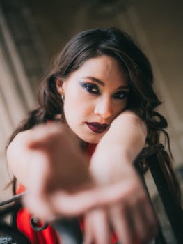 A stylish woman with dramatic makeup extends her hand towards the camera.