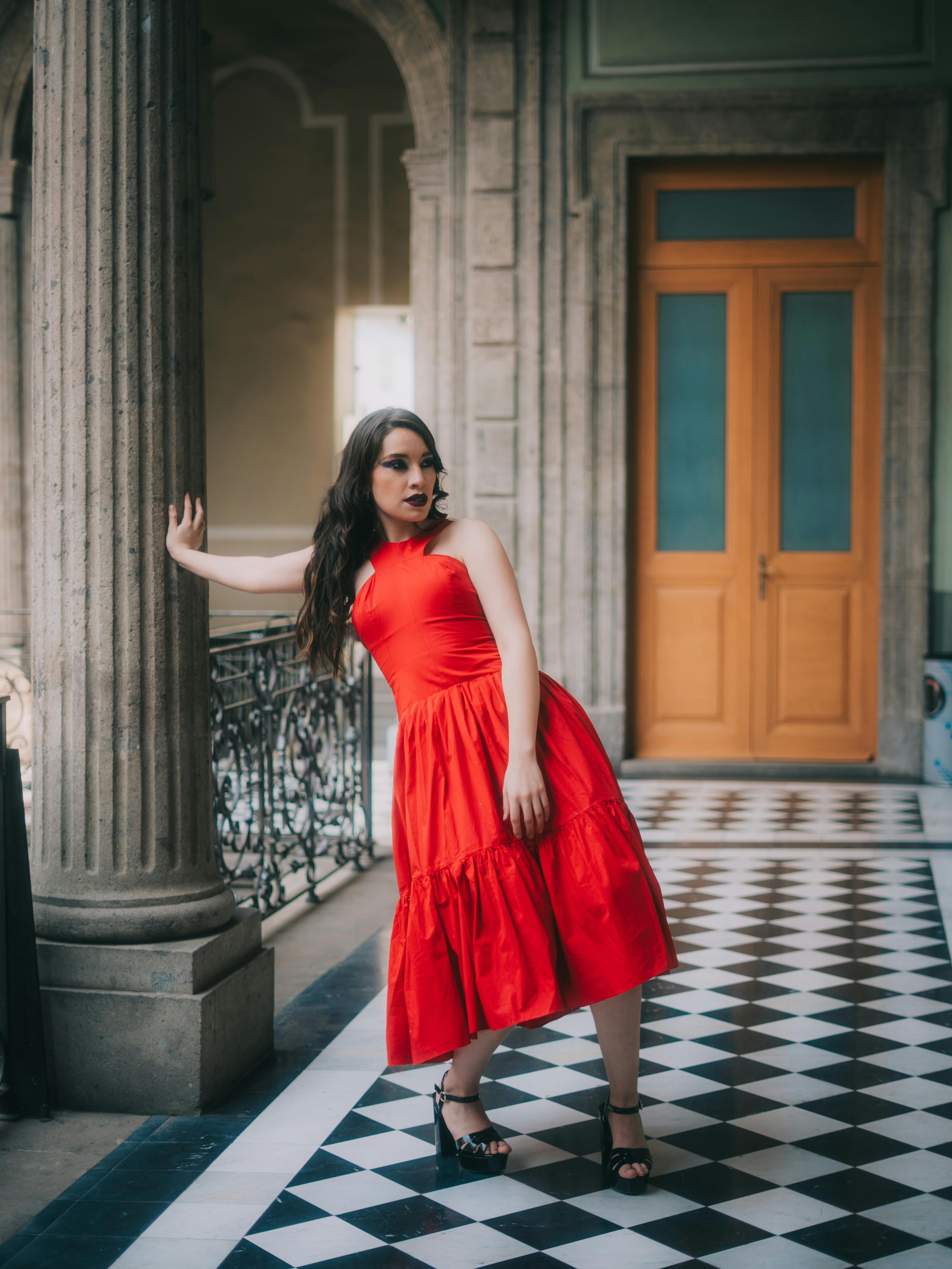 Free Striking pose of a fashion model in a vibrant red dress in a historical building. Stock Photo
