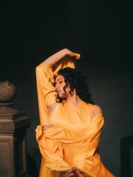Woman in a striking yellow dress poses gracefully indoors, bathed in warm light.