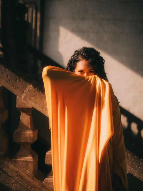Free A woman shrouded in yellow fabric, casting a mysterious gaze, lit by warm sunlight. Stock Photo
