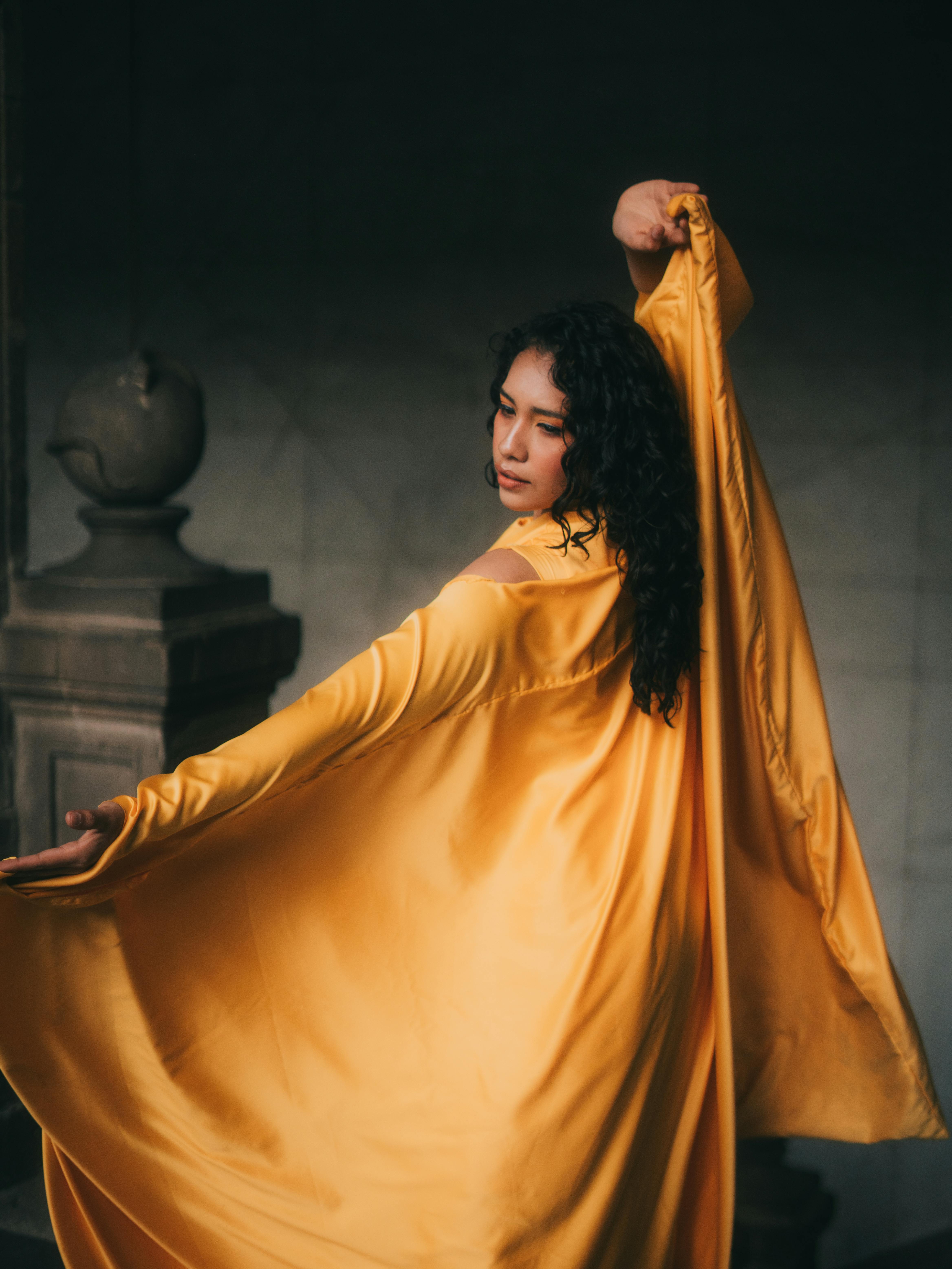 Zadarmo Štýlová modelka vo splývavých žltých šatách, ktorá elegantne pózuje v interiéri. Fotka z fotobanky