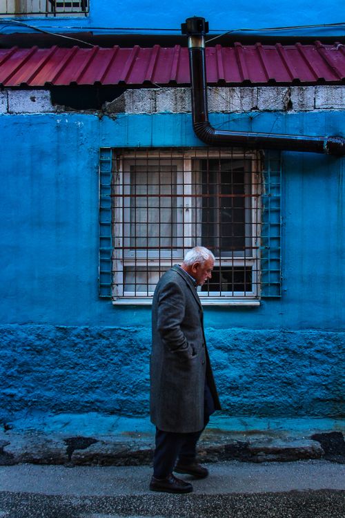 Free Elderly man strolling by a vivid blue wall, deep in thought. Urban scene with rich colors. Stock Photo