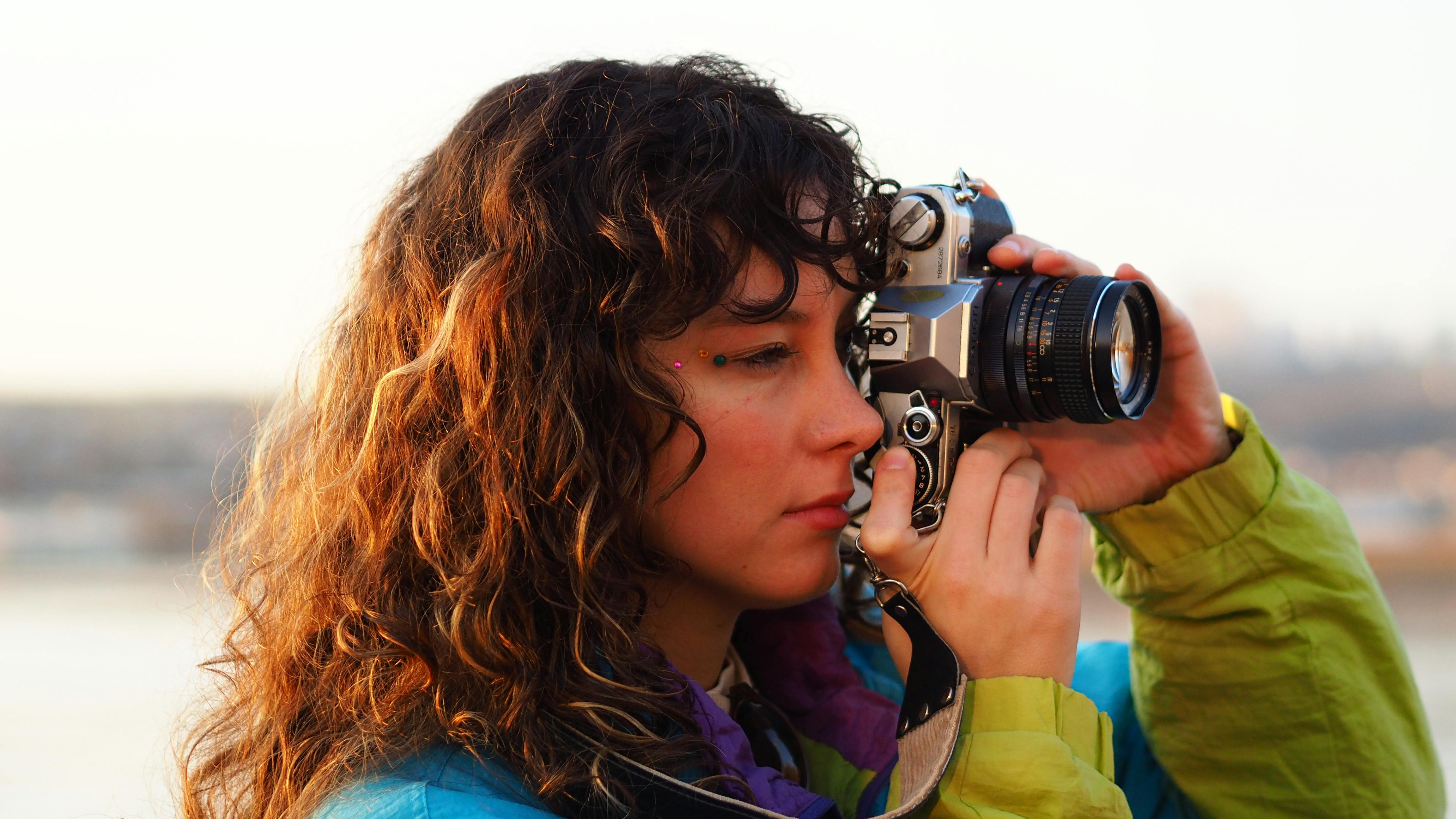 A young woman taking a photograph with a vintage camera during the day.