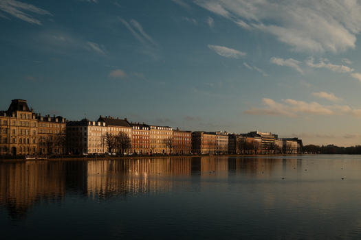 Elegant architecture reflected in still lake water under soft sky in Copenhagen.