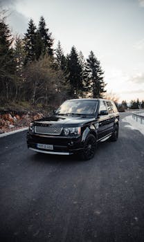 Black luxury SUV captured on a scenic road near Sarajevo, surrounded by evergreen trees at sunset.