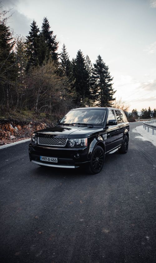 Free Black luxury SUV captured on a scenic road near Sarajevo, surrounded by evergreen trees at sunset. Stock Photo