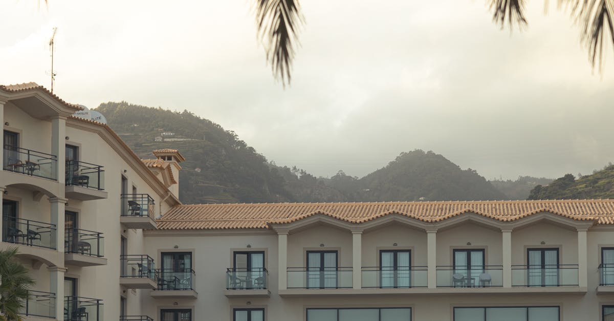 Photo by Cast.pics Modern hotel facade with pool, surrounded by palm trees and mountains.