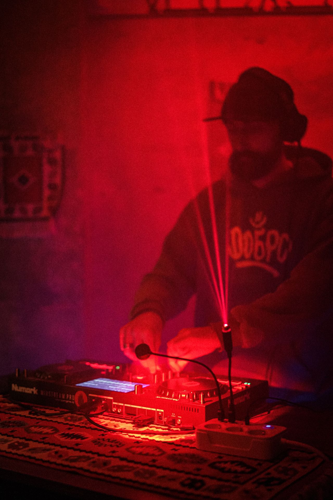DJ in dark club setting with red lights and laser effects