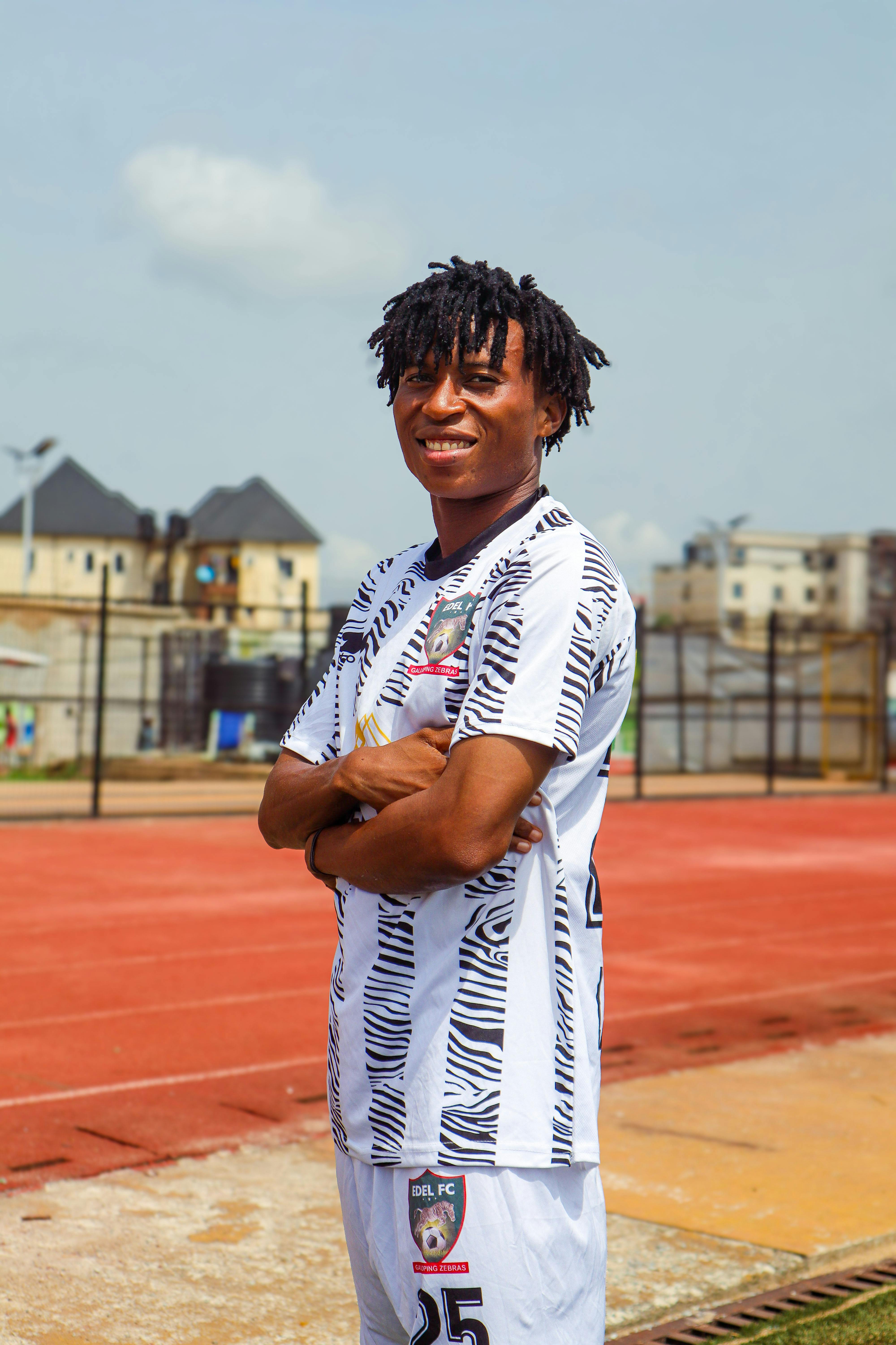 Young soccer player smiling confidently on a sunny track field. Urban background.