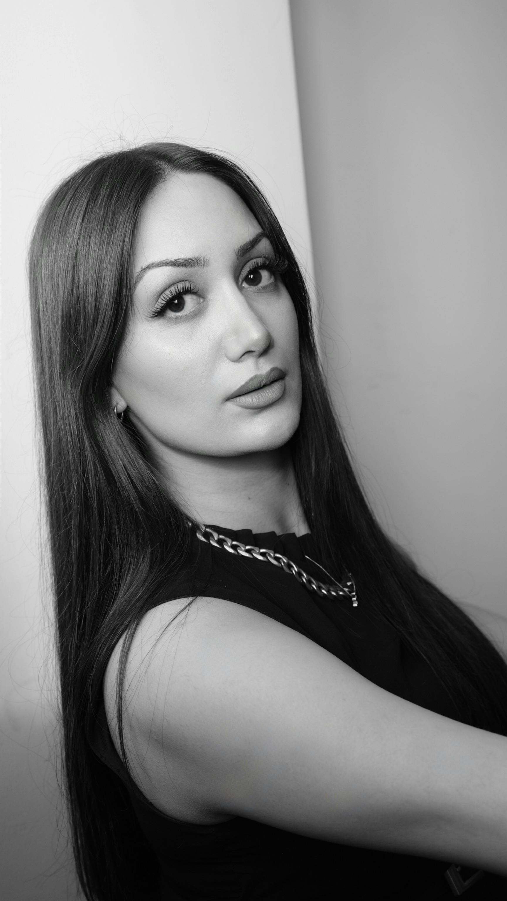Elegant black and white portrait of a woman with long hair, wearing a chain necklace.