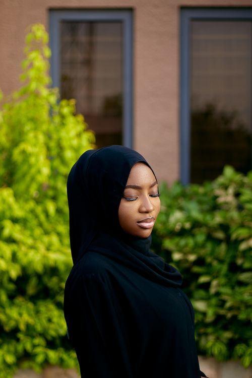 Free Portrait of a woman in a black hijab, eyes closed, with a lush green background. Stock Photo