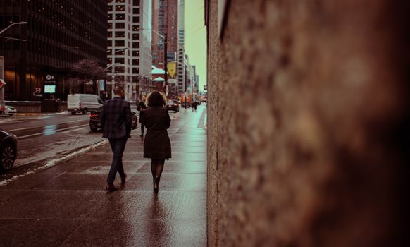 A couple walking on a wet sidewalk in downtown Toronto during winter, creating an urban atmosphere.