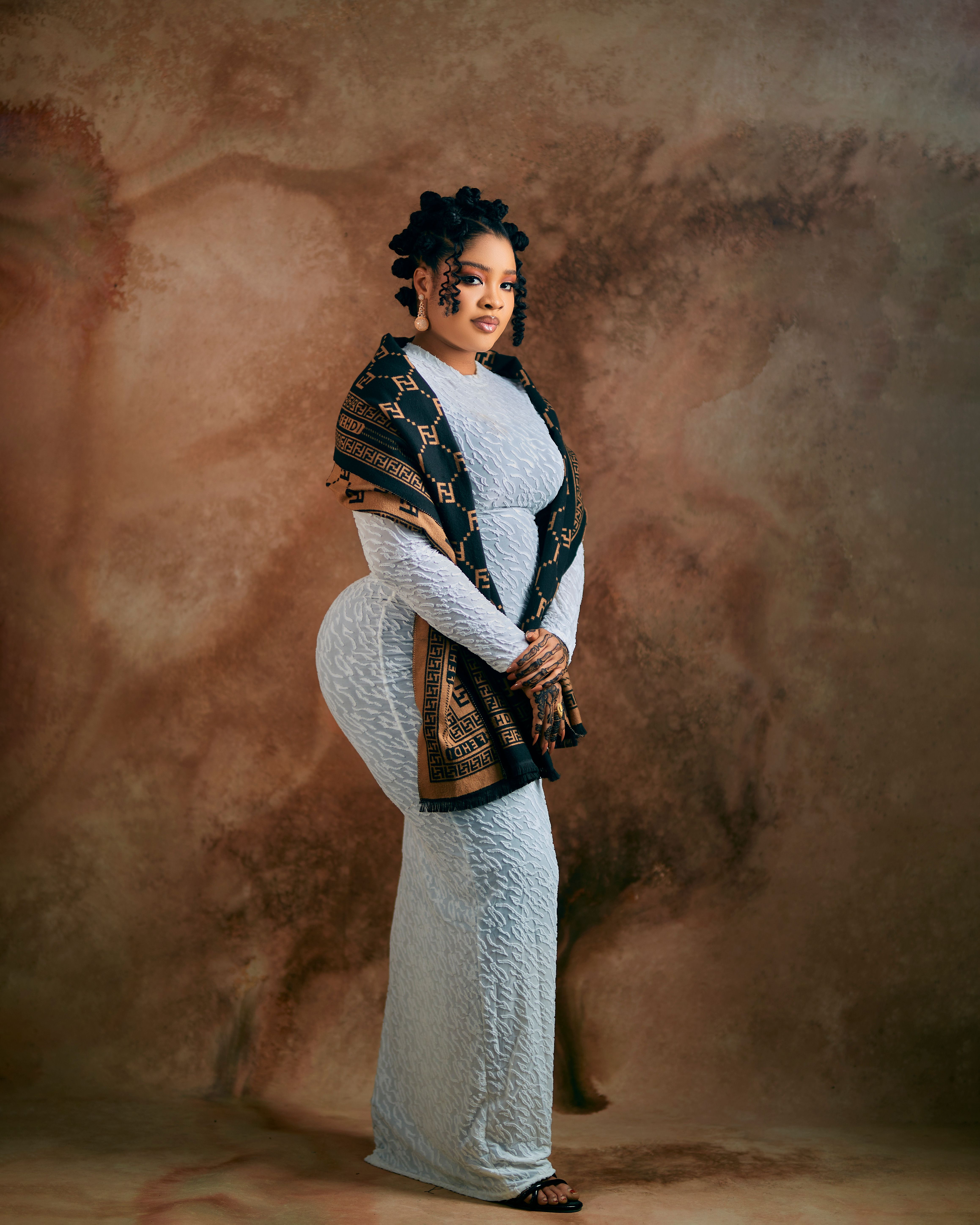 Portrait of an elegant woman wearing a traditional ornate shawl and dress against a textured background.