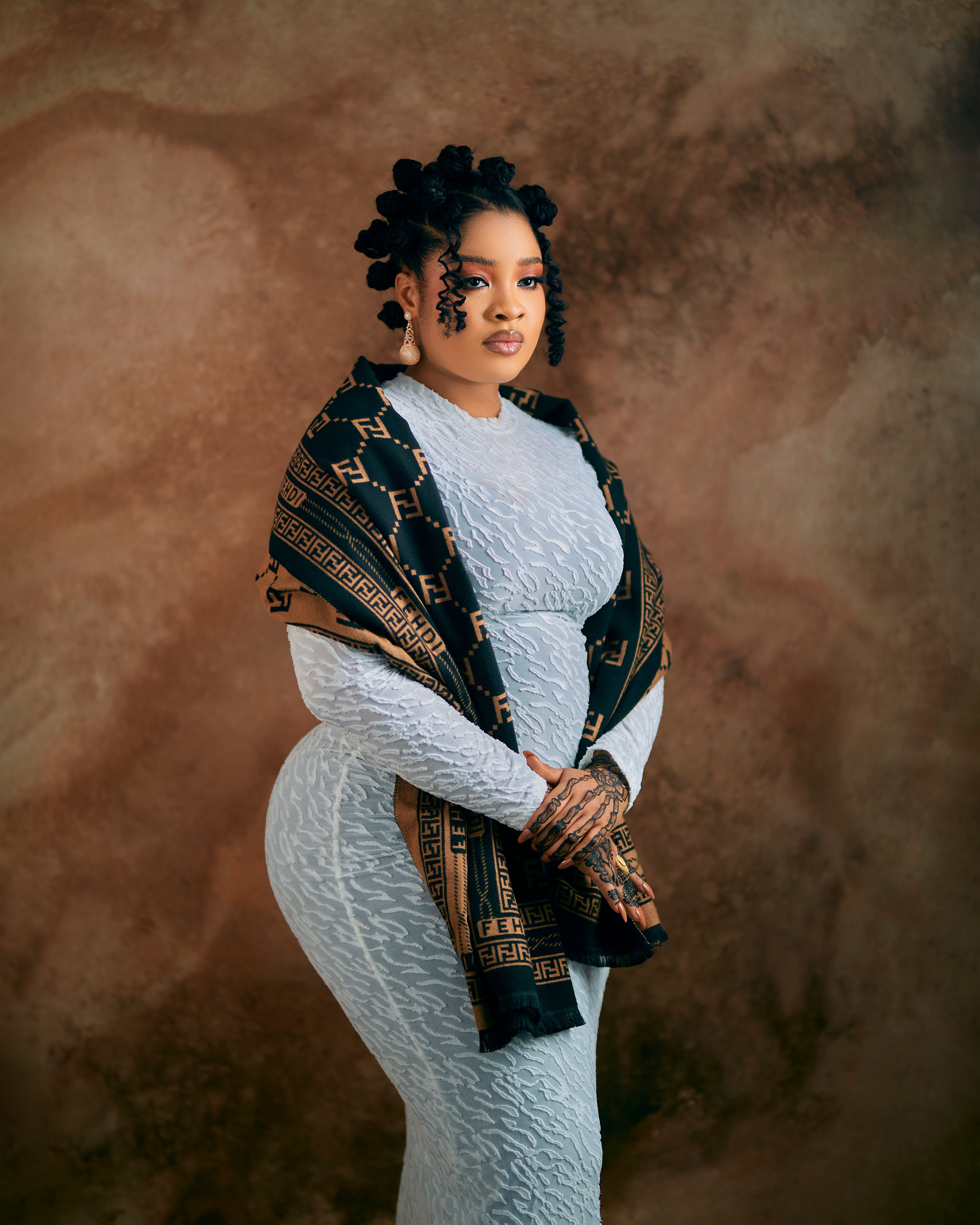 Stylish woman poses gracefully in elegant traditional attire against textured background.
