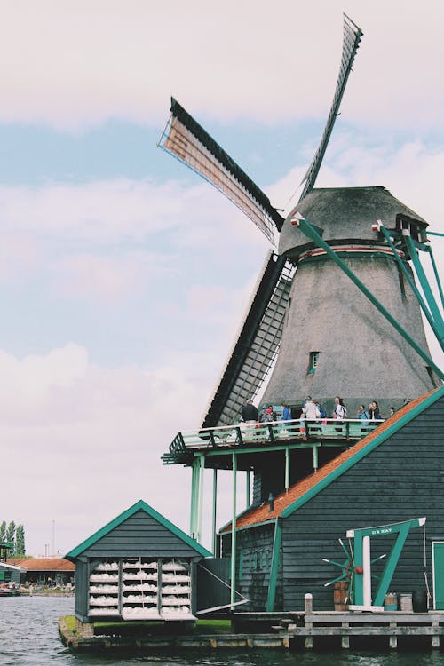People Walking on Windmill Near Body of Water
