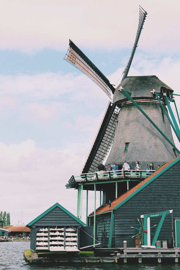 People Walking On Windmill Near Body Of Water