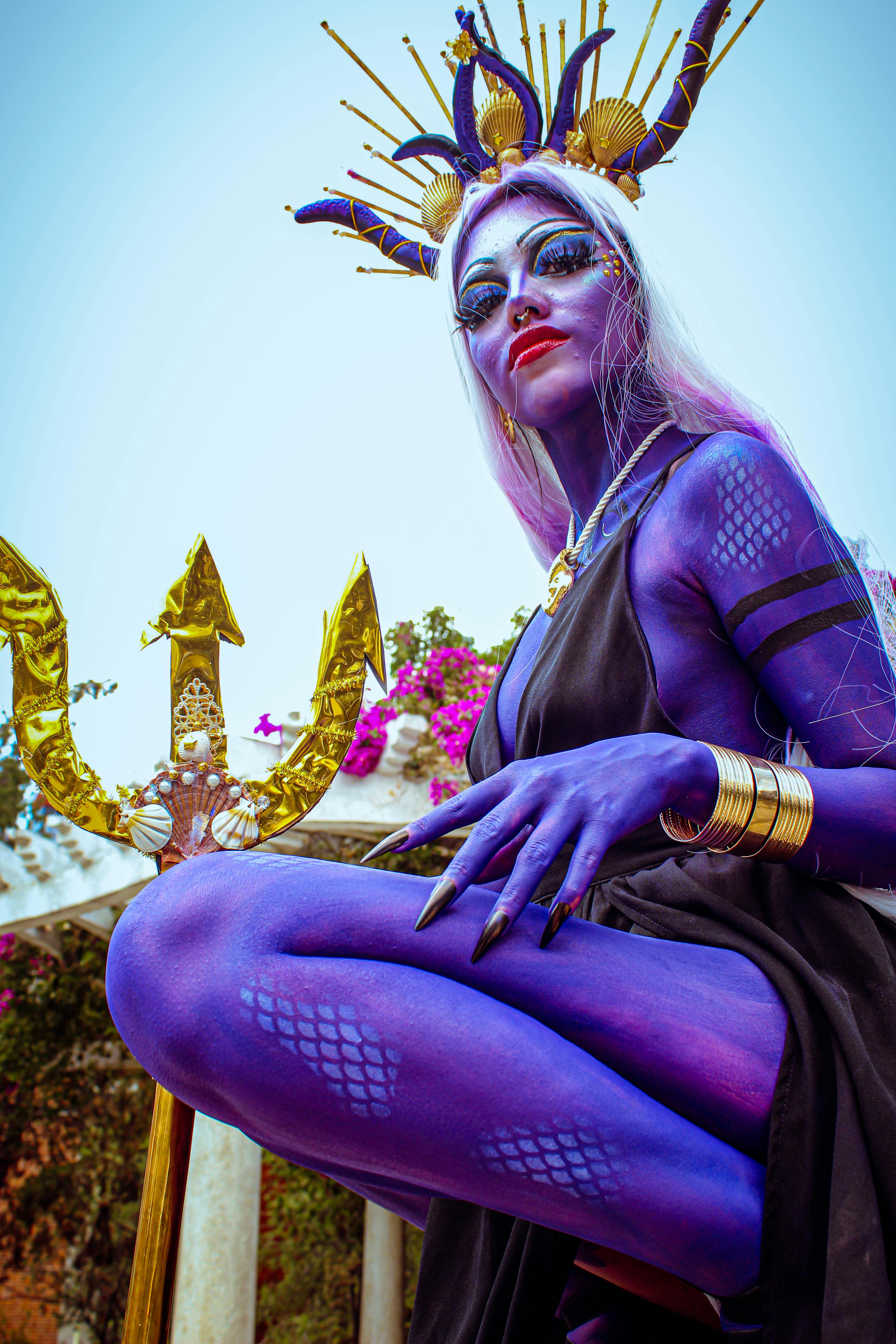Vibrant fantasy cosplay featuring a model with vivid body paint and an elaborate headdress holding a trident.
