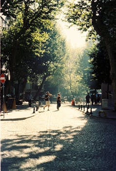 Pedestrians walk down a charming cobblestone street in Istanbul, basking in warm, dappled sunlight.