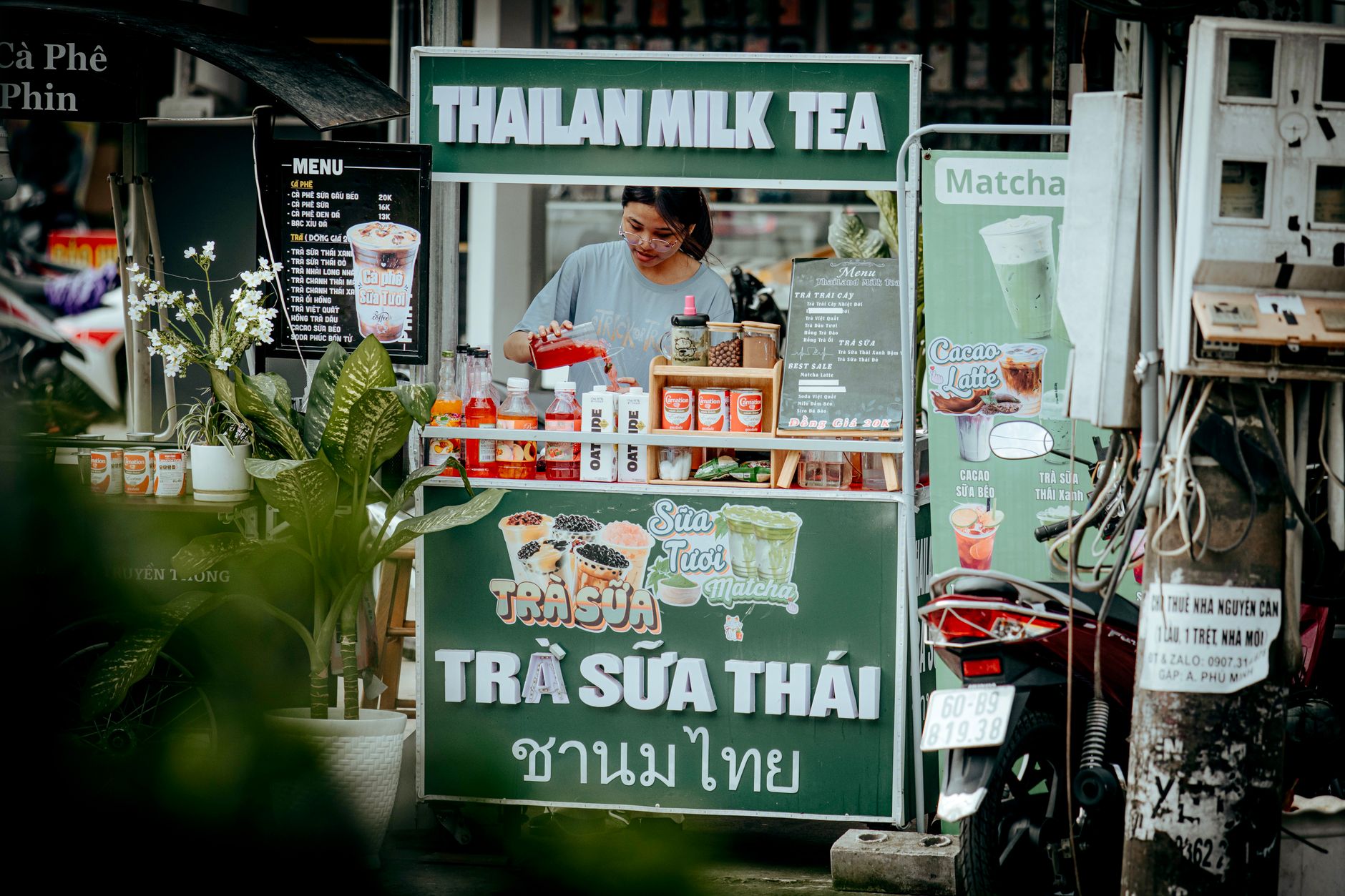 Vendor preparing drinks at a Thai milk tea stand in an outdoor setting.