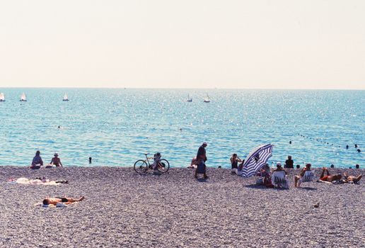 Relaxing summer day at a vibrant beach in Antalya, Türkiye with sunbathers and boats.