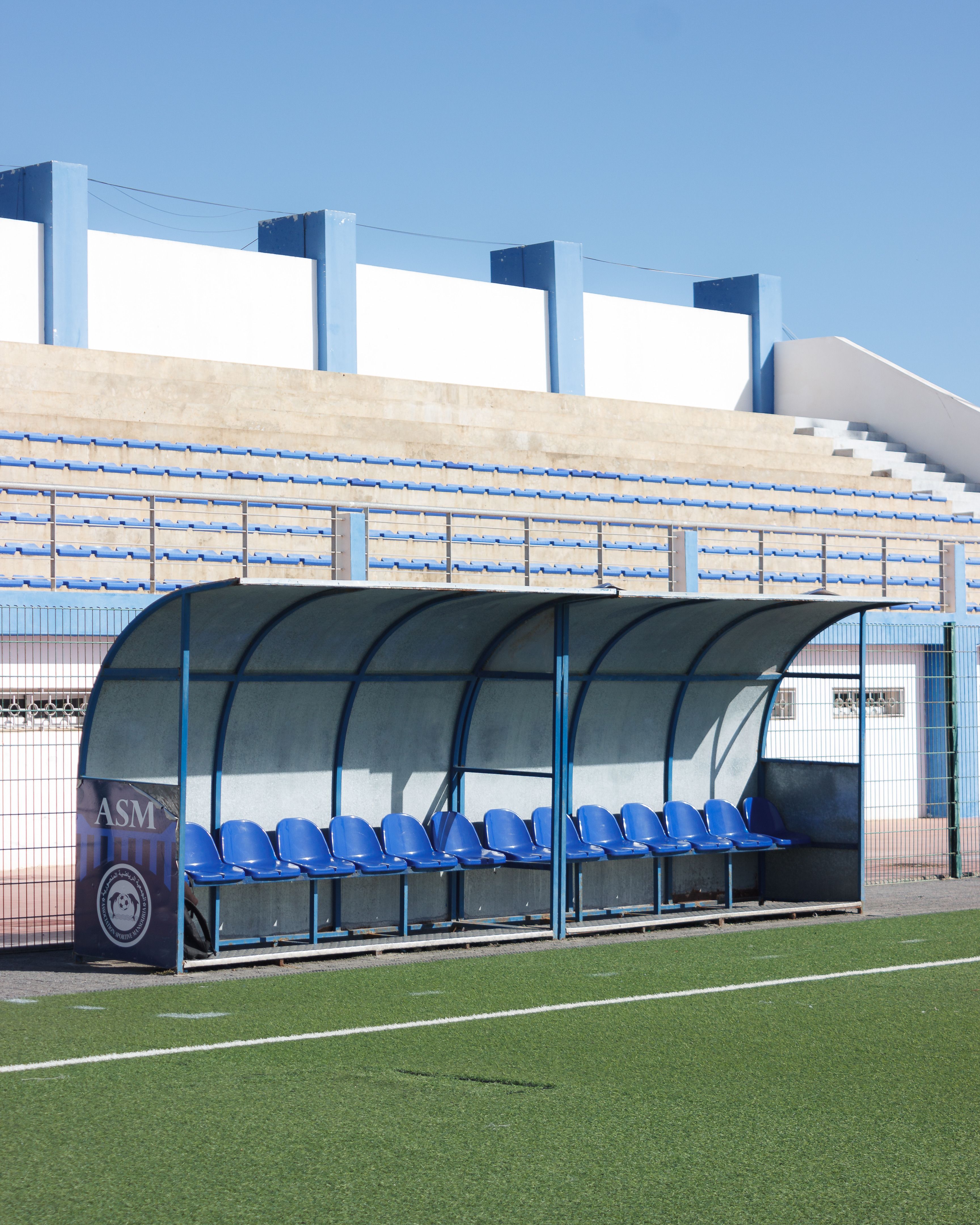 Outdoor soccer field with empty bench seating and clear sky.