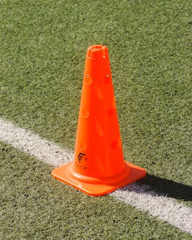 A vibrant orange traffic cone placed on a synthetic grass sports field.