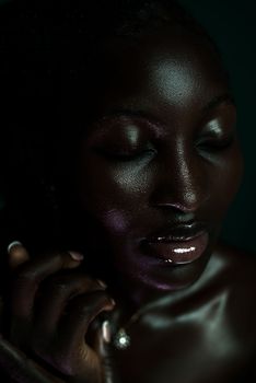 A captivating close-up portrait of a woman with glistening dark skin against a dark backdrop.