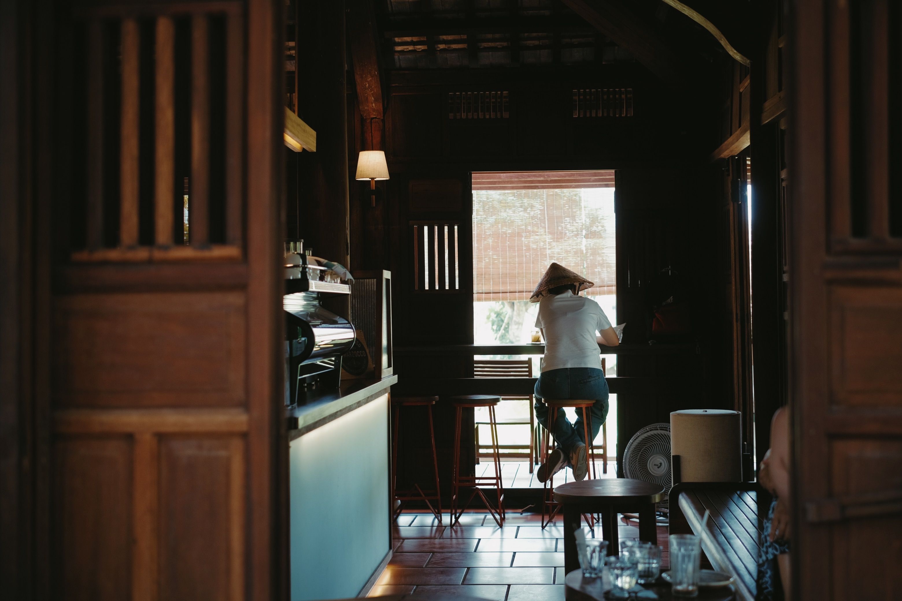 A serene coffee shop interior featuring a lone patron enjoying a quiet moment by the window.
