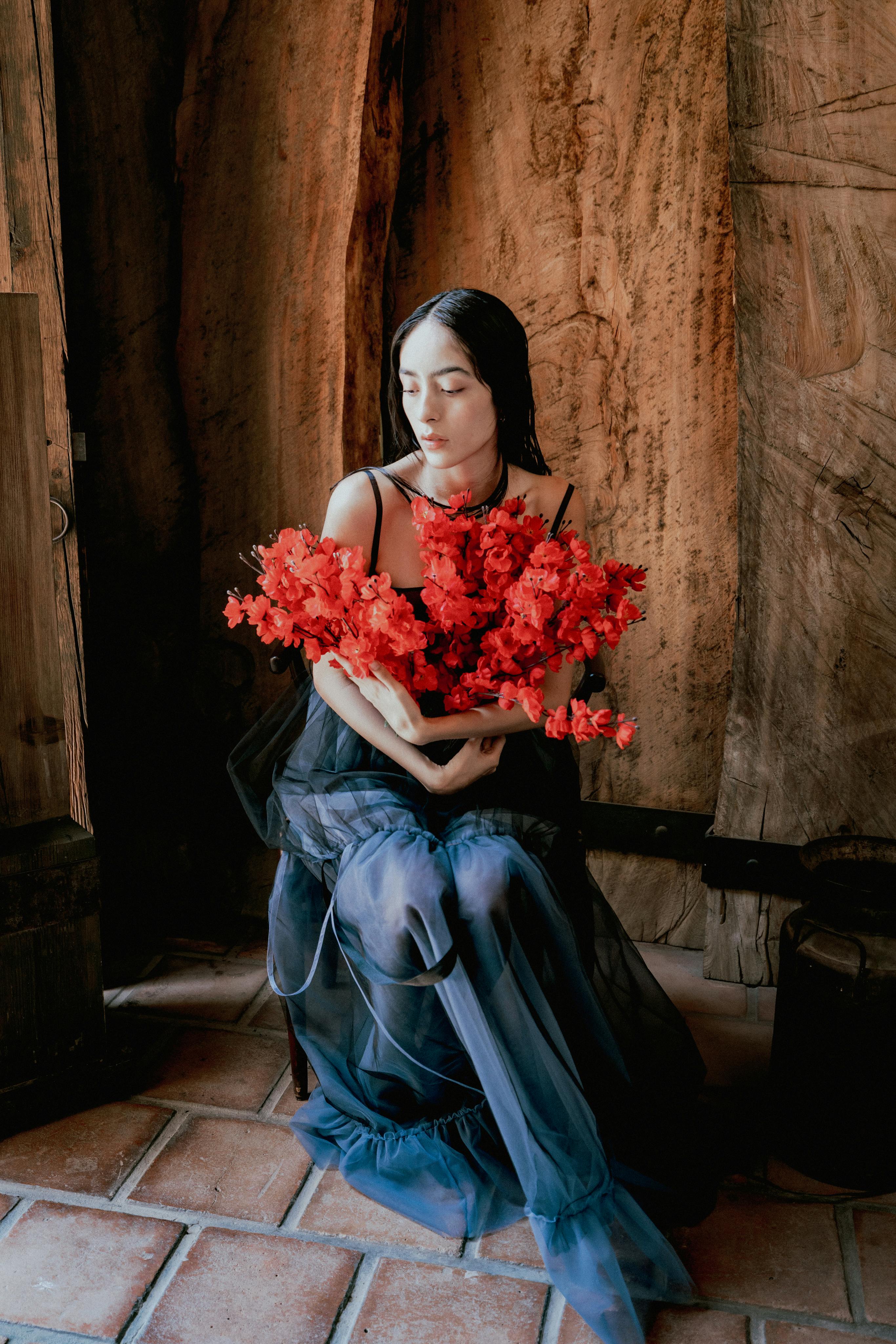 A woman in a black dress holds a bouquet of vibrant red flowers in an intimate indoor setting.