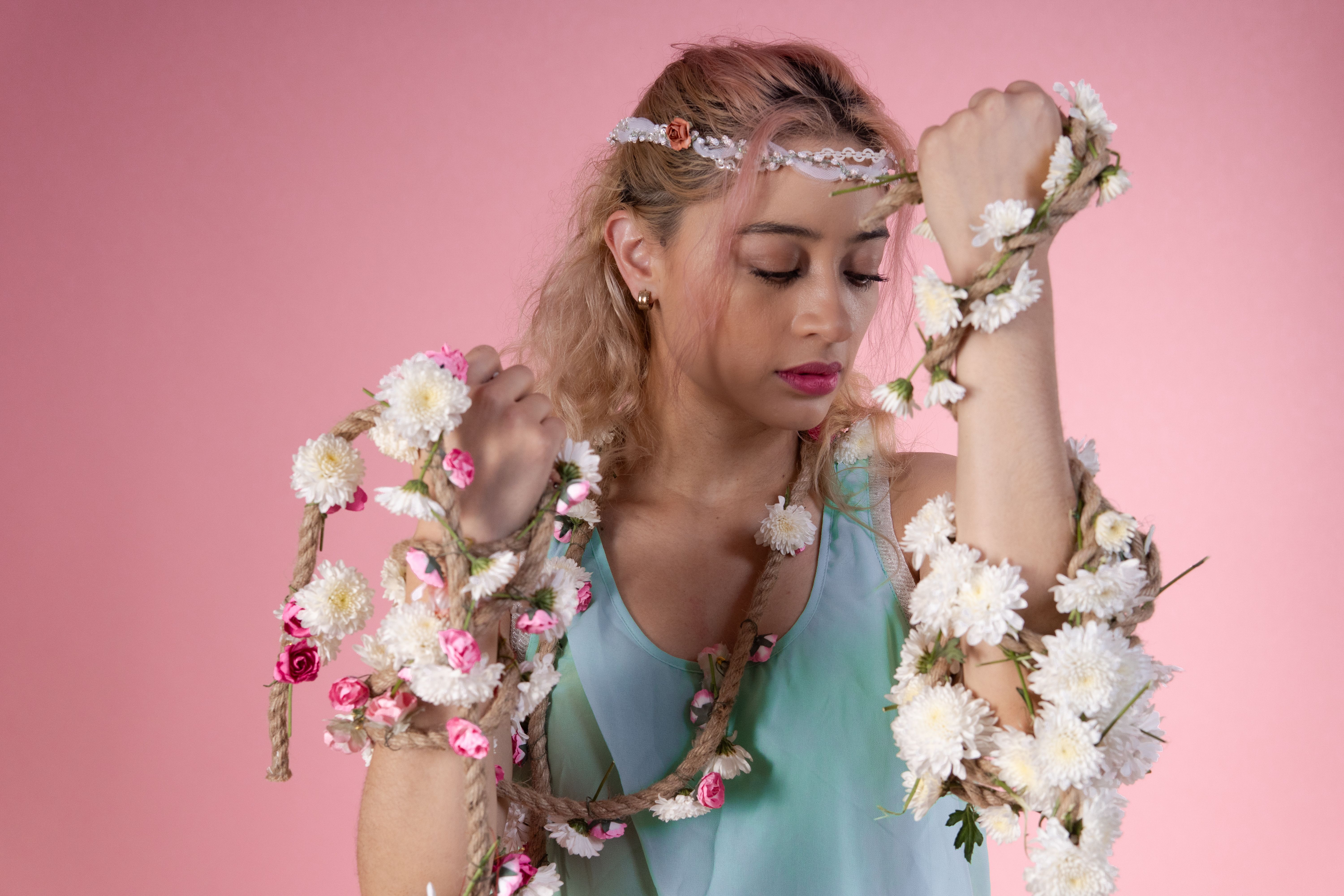 A graceful woman in a floral arrangement poses against a pink backdrop.