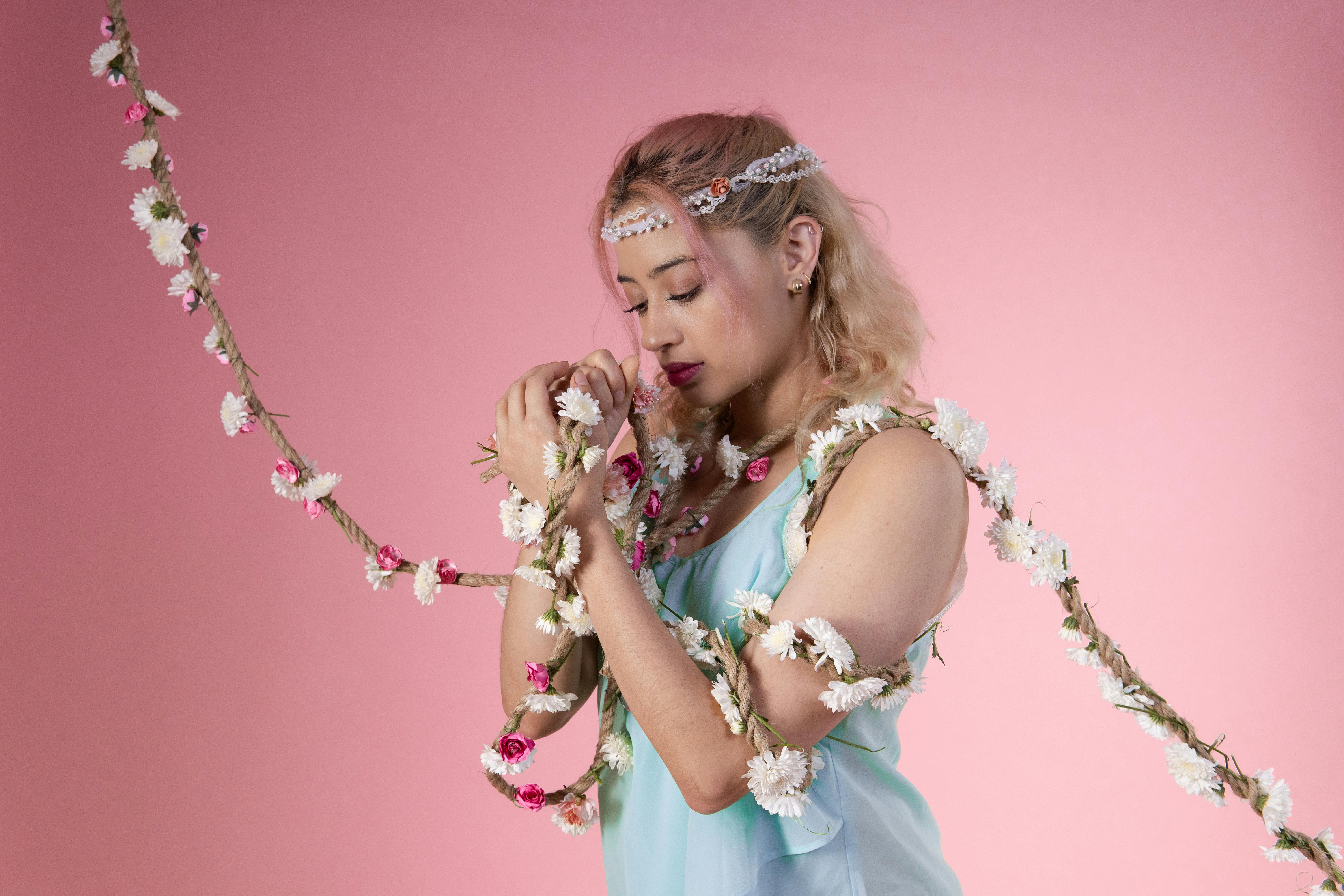 A contemporary dancer wrapped in a delicate floral garland, set against a soft pink background.