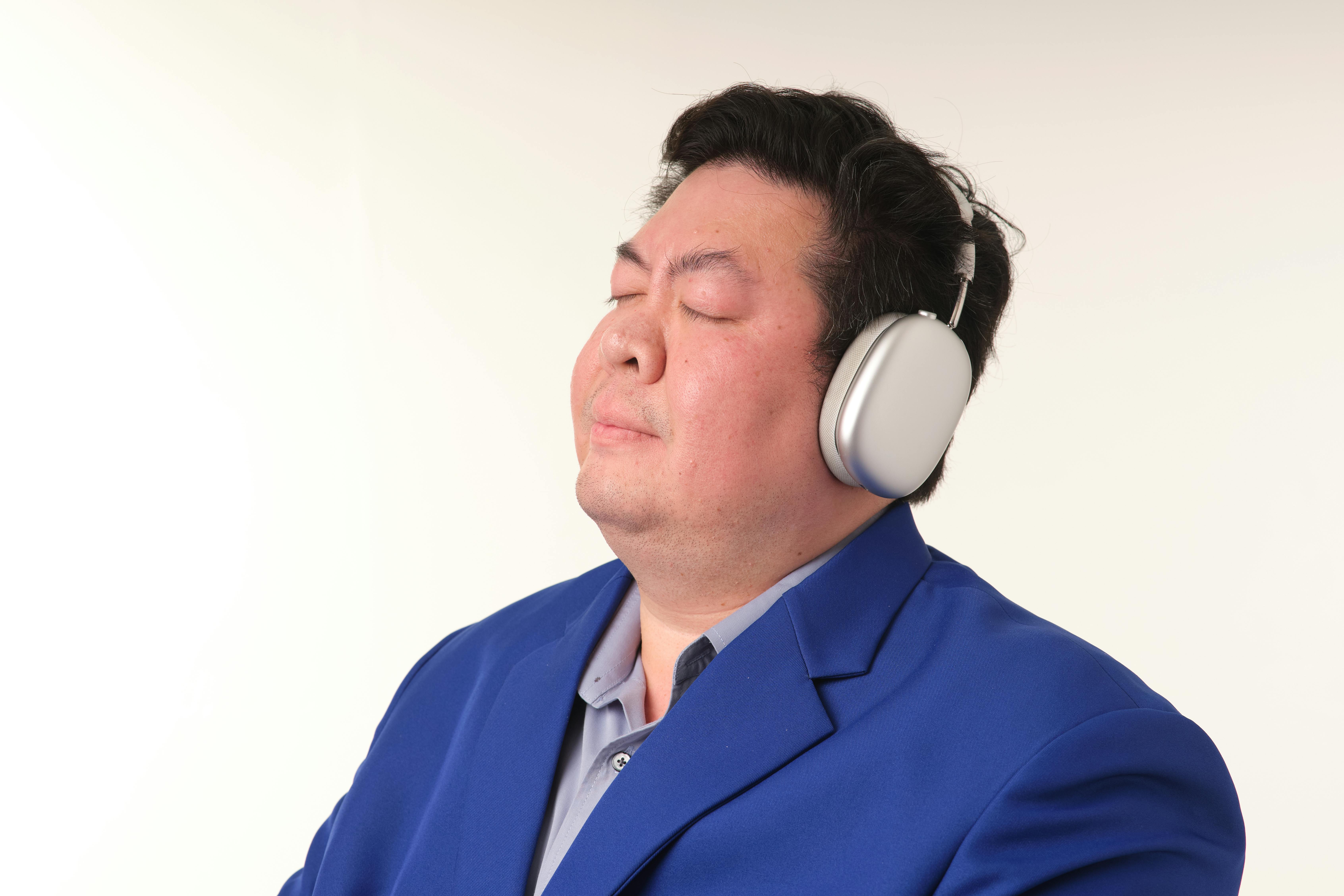 무료 파란색 정장을 입고 헤드폰을 끼고 음악을 즐기는 성인 남성. 차분하고 여유로운 표정. 스톡 사진