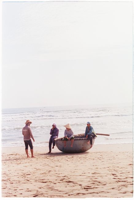 Four fishermen with a traditional round basket boat on a sandy beach, sunny day.