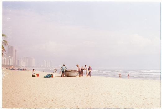 People enjoying a sunny beach day with city skyline and sandy shores.