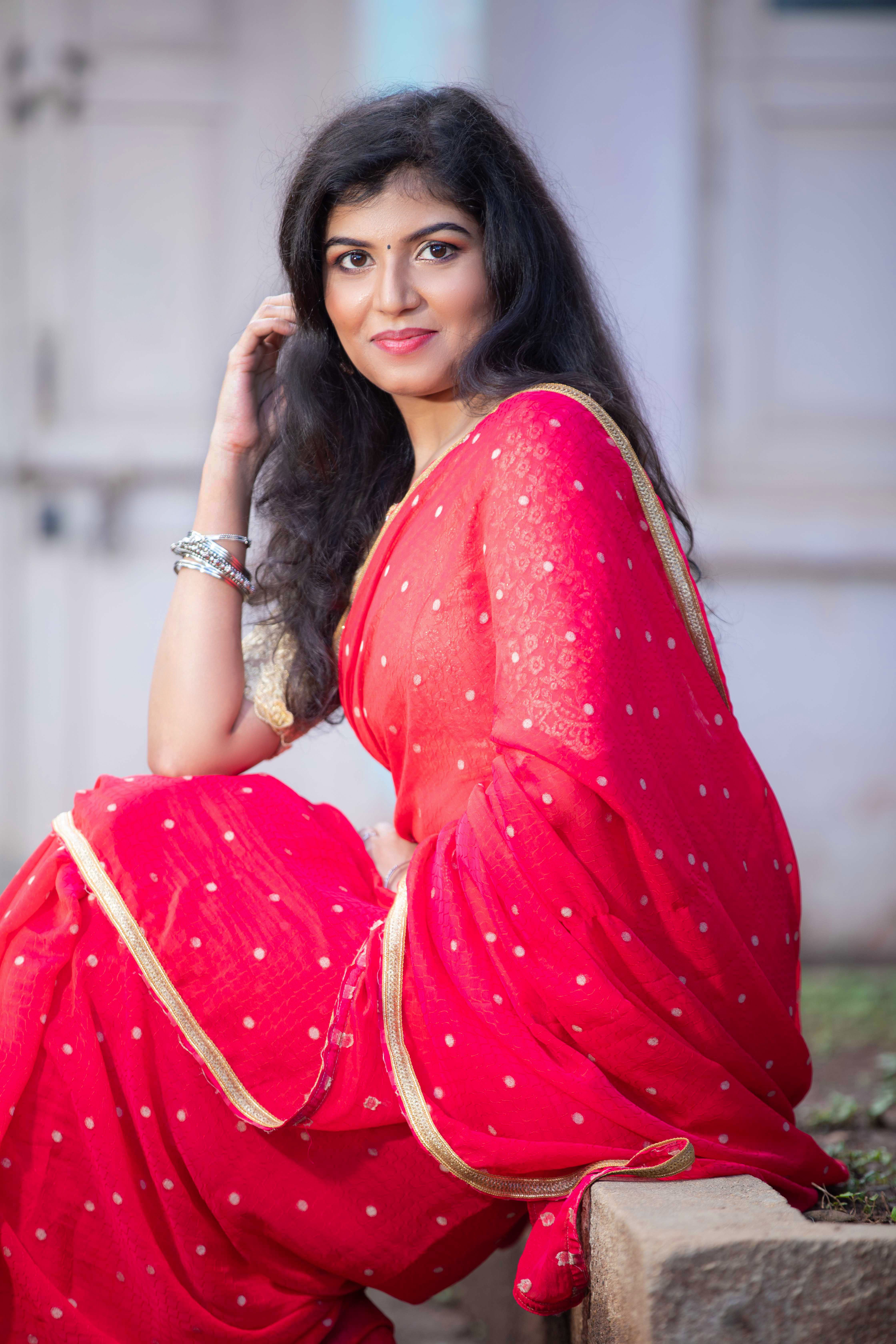 Charming portrait of an elegant woman in a traditional red saree, outdoors in Bengaluru.