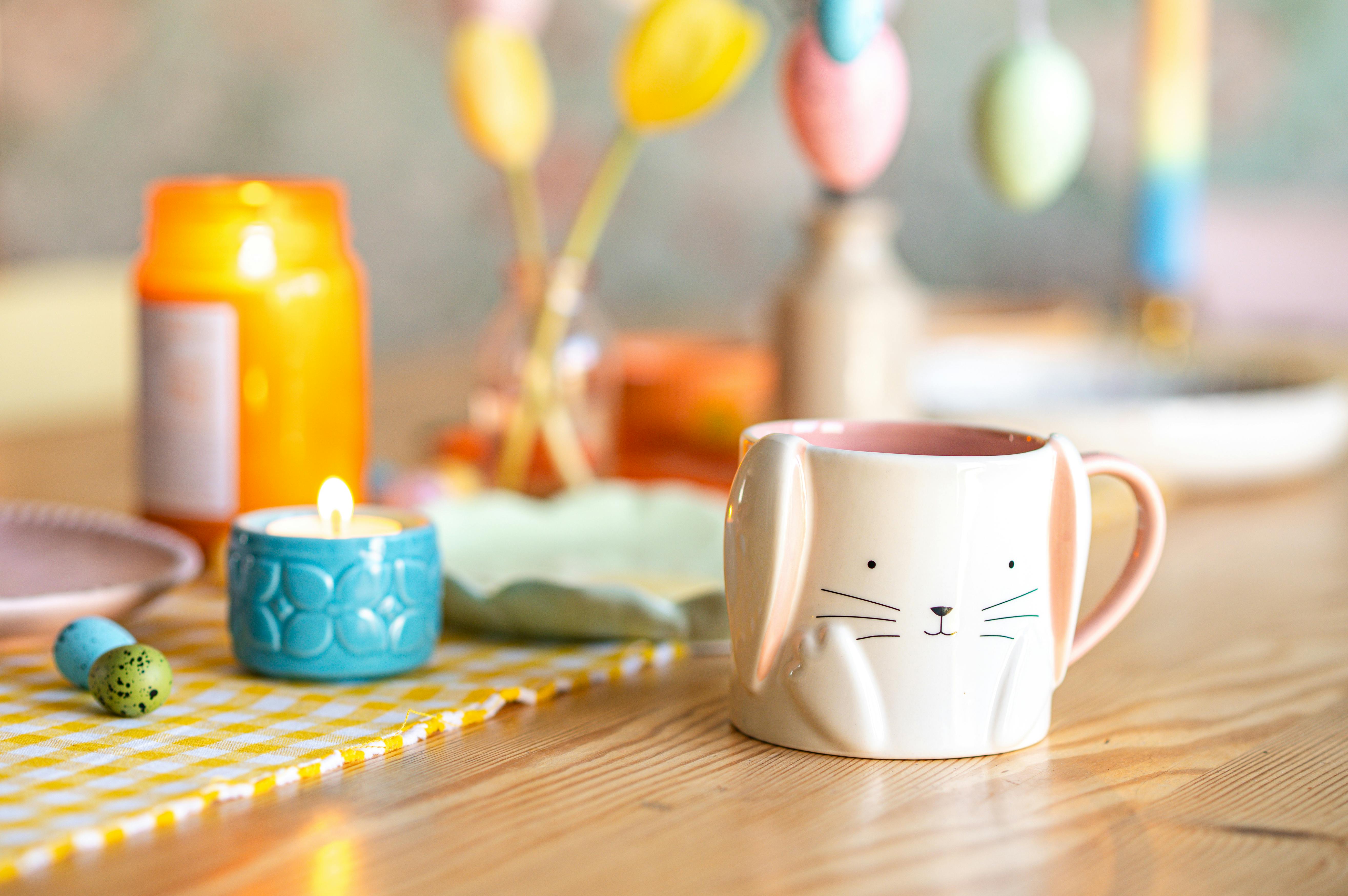 Easter-themed setup with a bunny mug, candle, and colorful decor on a wooden table.