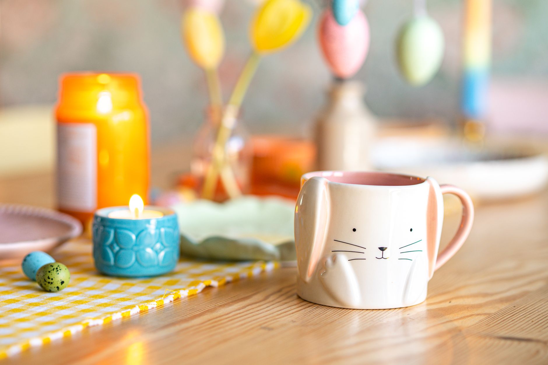 Easter-themed setup with a bunny mug, candle, and colorful decor on a wooden table.