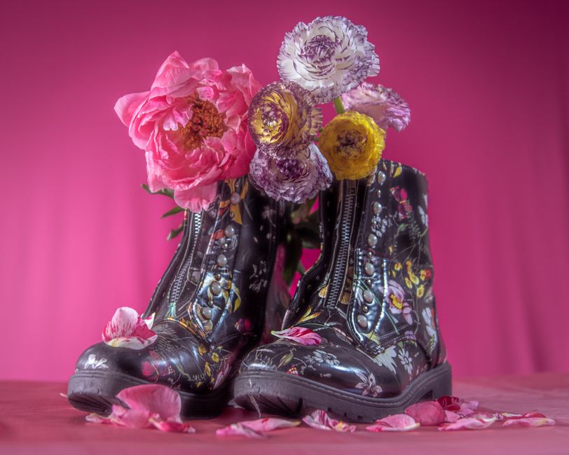 Decorative floral boots filled with colorful blooms on a vivid pink backdrop. Stylish and artistic fashion display.