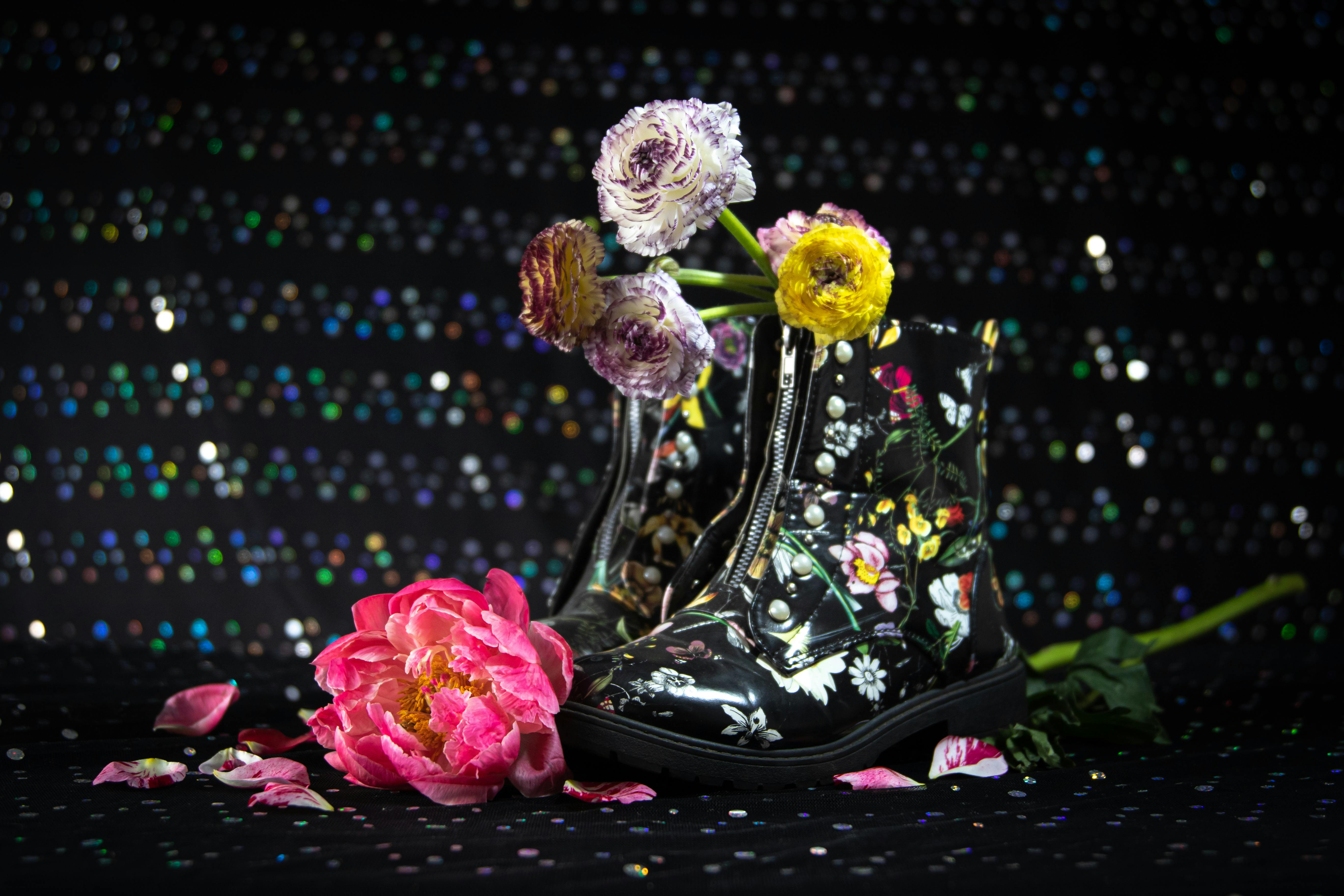 在闪闪发光的背景下，一双时尚的黑色靴子装饰着花卉图案和五颜六色的花朵