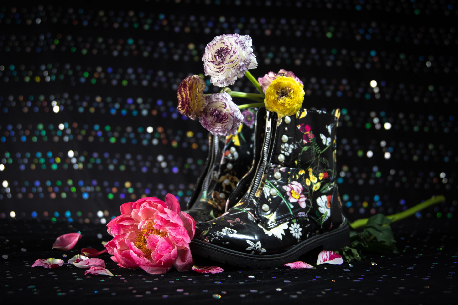 Stylish black boots adorned with floral patterns and colorful blossoms set against a sparkling backdrop.