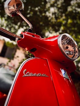 Vibrant red Vespa scooter headlight and emblem in focus, showcasing classic Italian design.